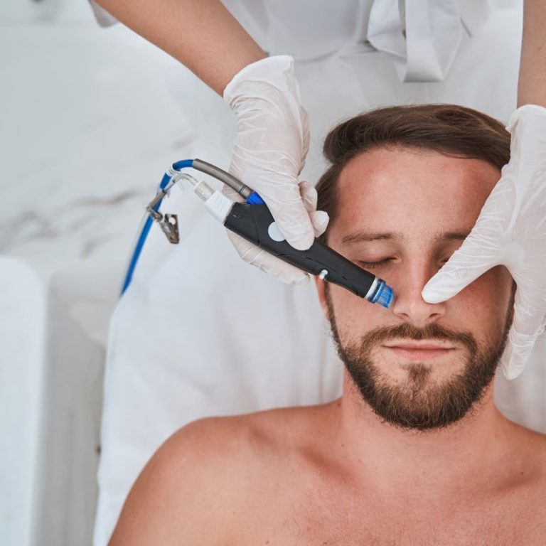 Top view of a handsome man lying with his eyes shut during the blackhead removal procedure performed by a doctor